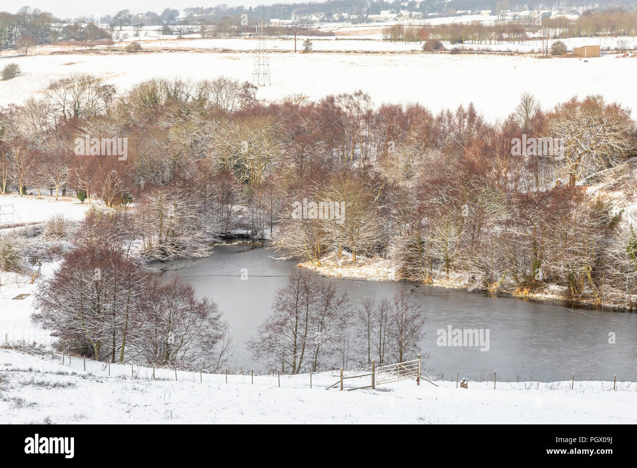 Tong Park dam, Baildon, Yorkshire in Winter. The fields are covered in snow and surrounding trees have a white dusting. Stock Photo