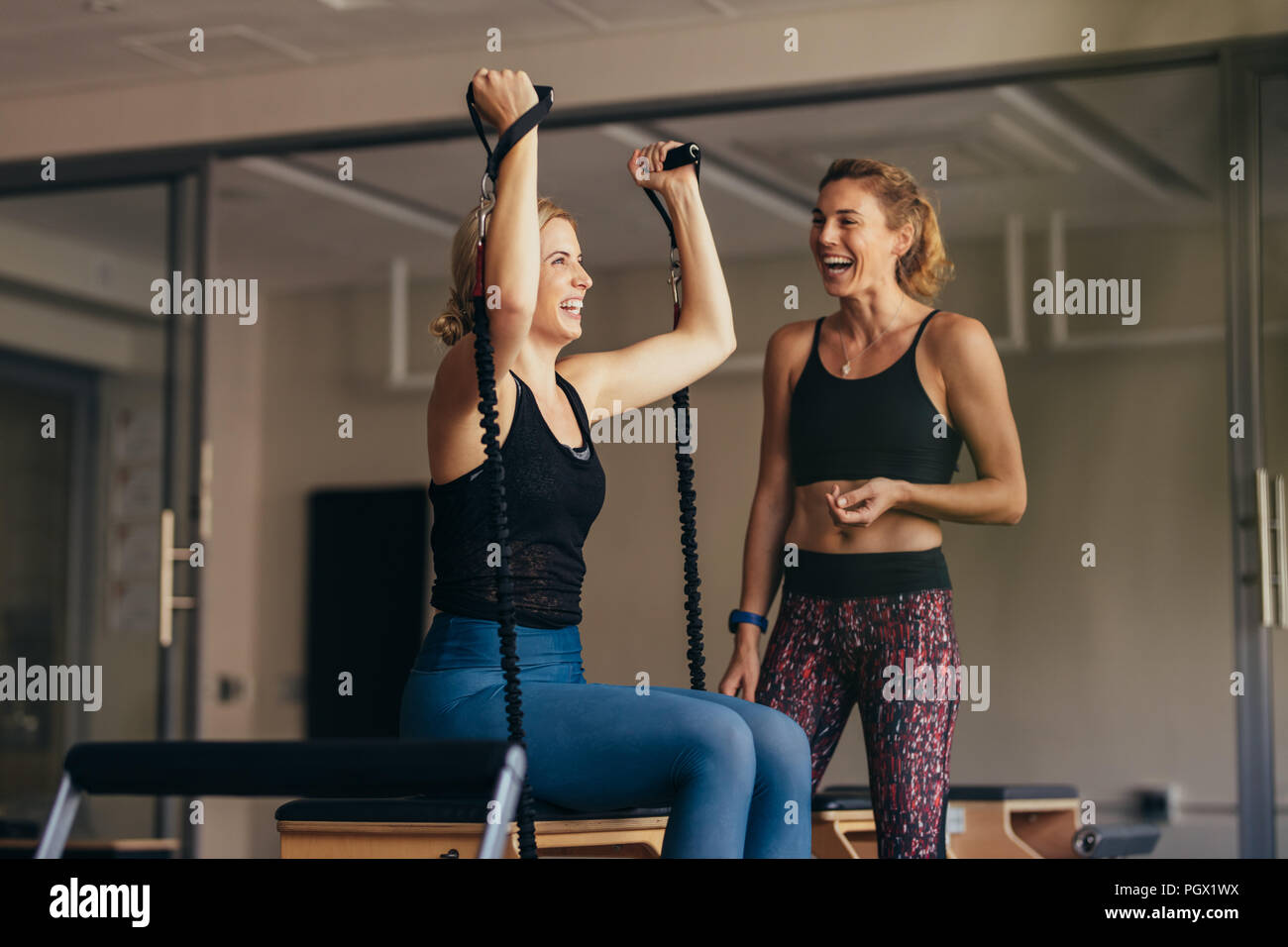 Smiling woman pulling stretch bands during her pilates training. Women at a pilates training gym laughing while doing workout. Stock Photo