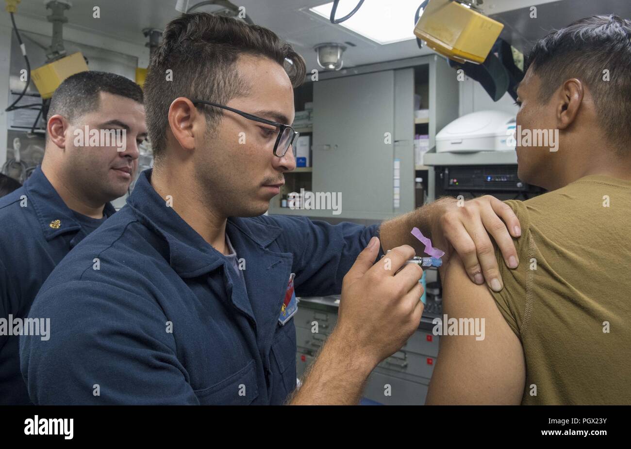 Seaman Santiago Arevalo-Mendoza administering a Japanese encephalitis vaccine to a Sailor aboard the Arleigh Burke-class guided-missile destroyer USS Benfold (DDG 65), East China Sea, August 22, 2018. Image courtesy Petty Officer 2nd Class Elesia Patten / U.S. Navy. () Stock Photo