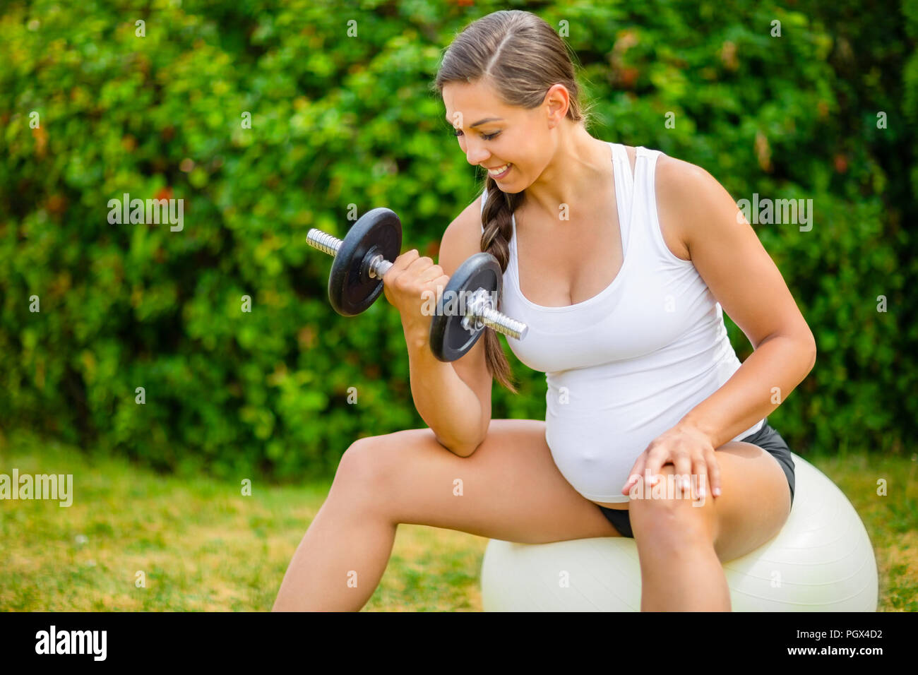 Healthy Pregnant Woman Lifting Weights On Exercise Ball In Park Stock Photo
