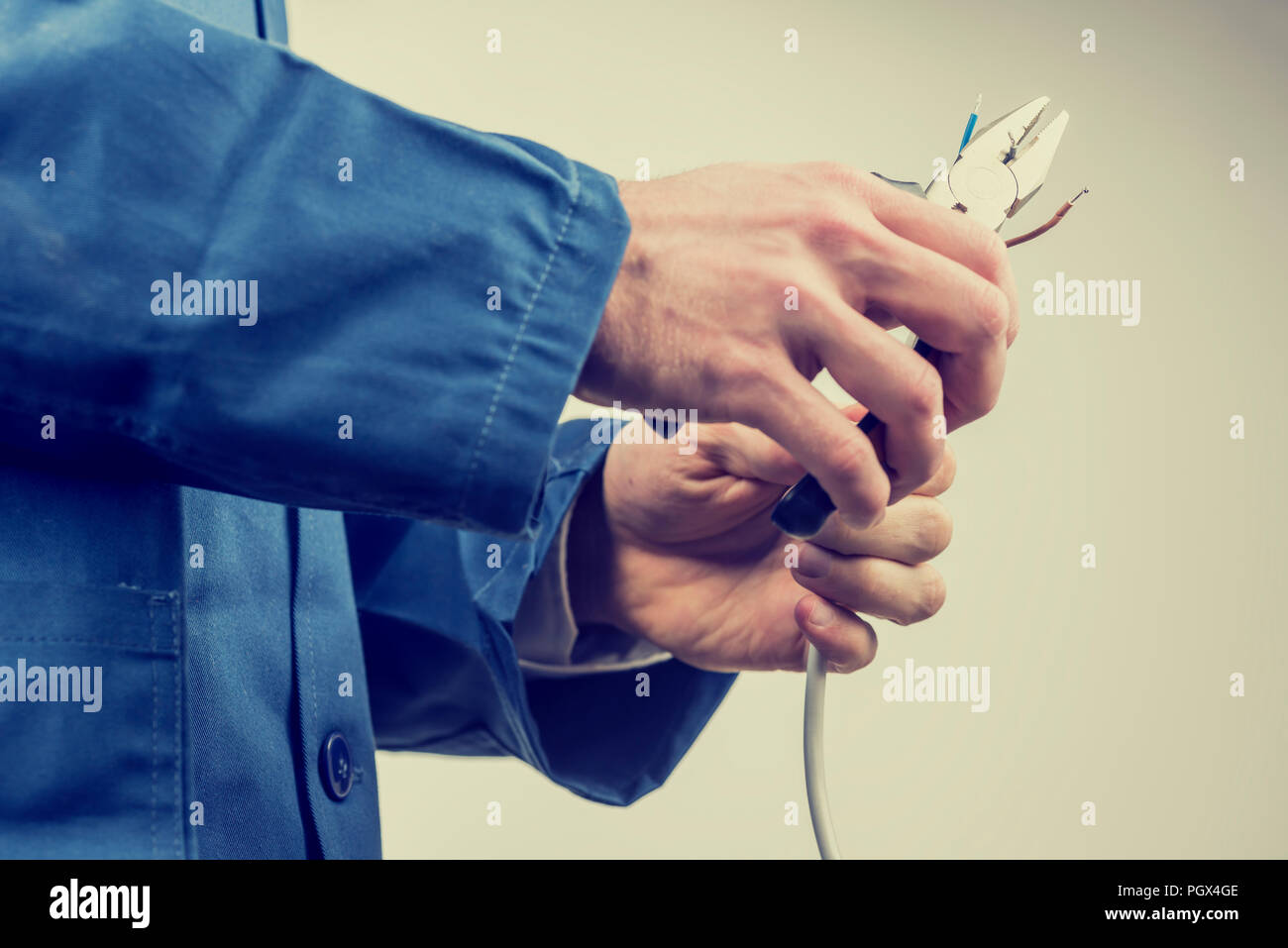 Workman in overalls repairing an electric cable or wiring using pliers while doing a domestic or industrial installation , maintenance or repairs, clo Stock Photo