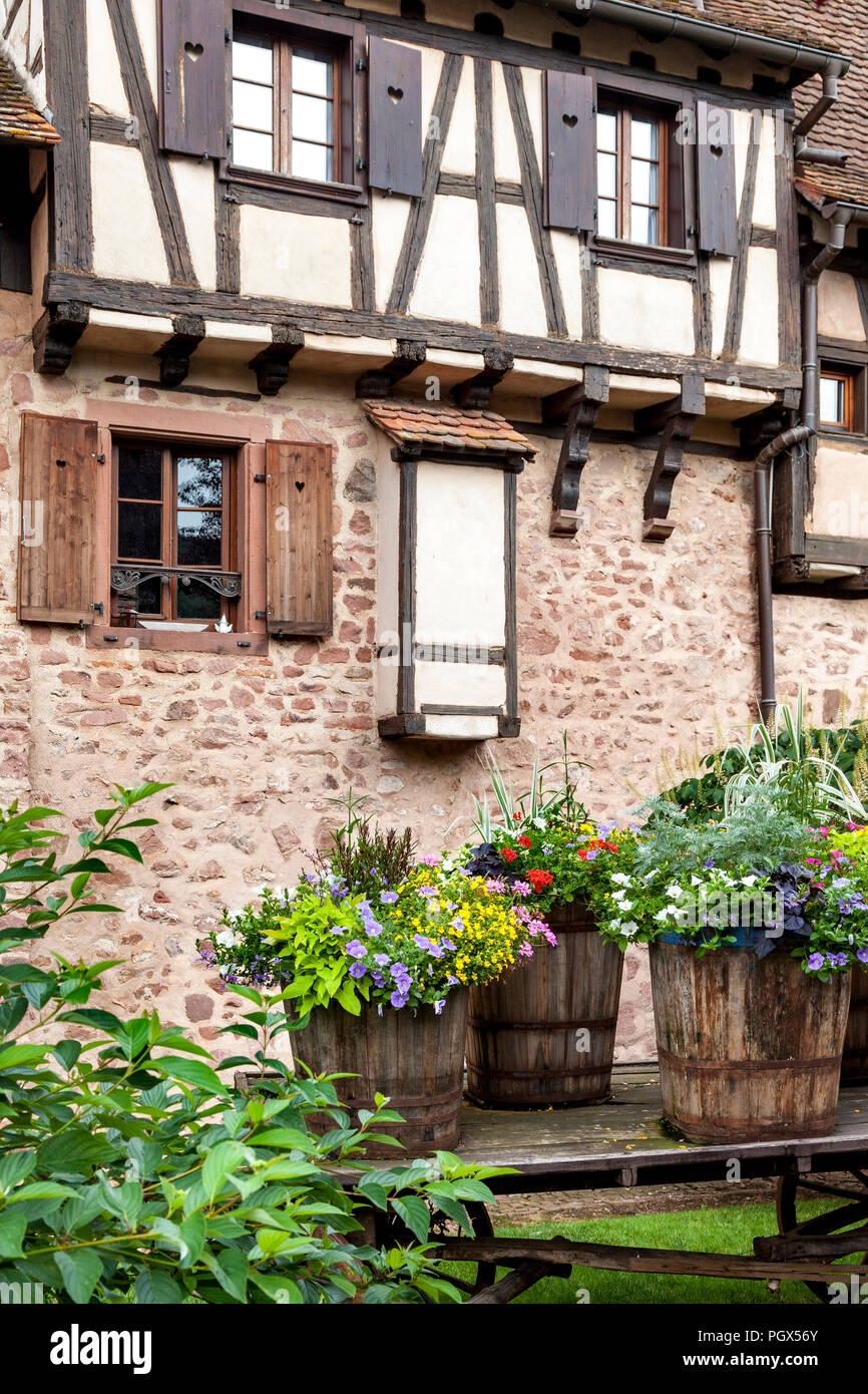 Flowers in barrel planters below a stone and half-timbered home in Riquewihr, Alsace, France Stock Photo