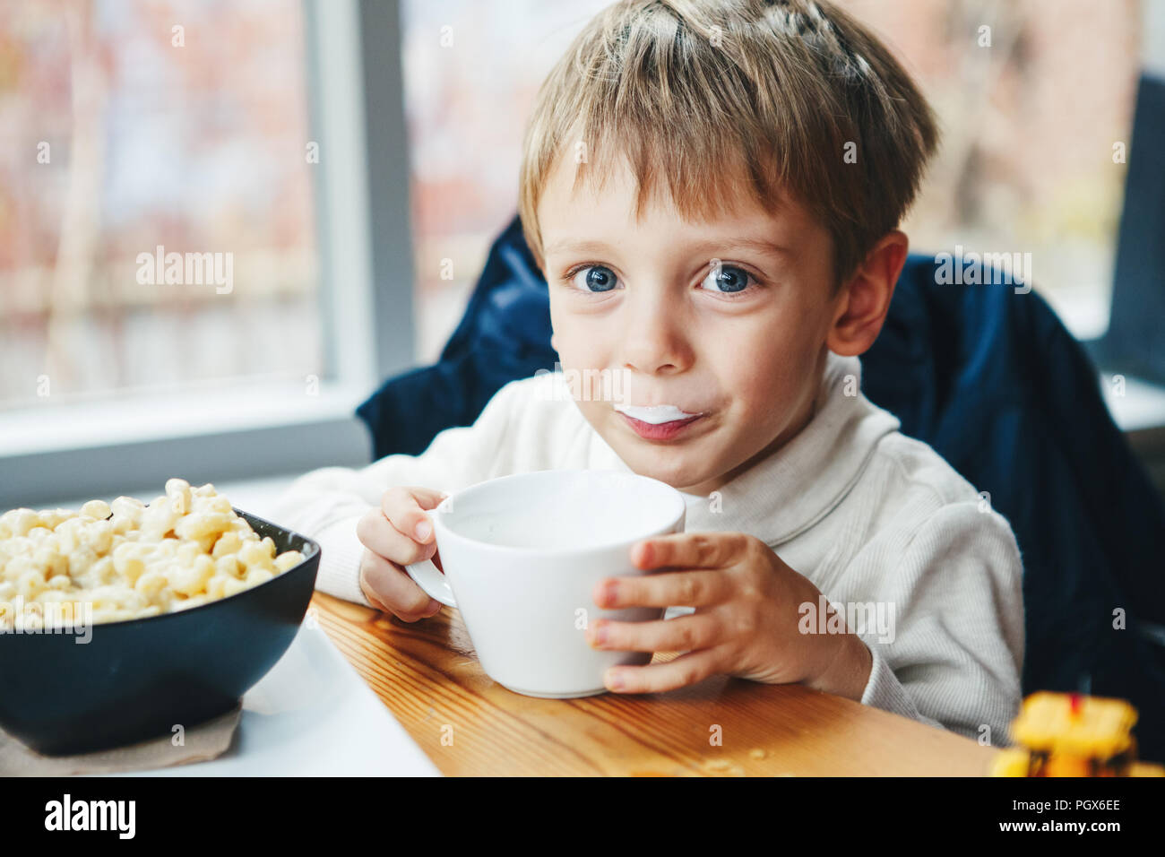 Portrait of cute adorable Caucasian child kid boy drinking milk from white cup eating breakfast lunch early morning, everyday lifestyle candid moments Stock Photo