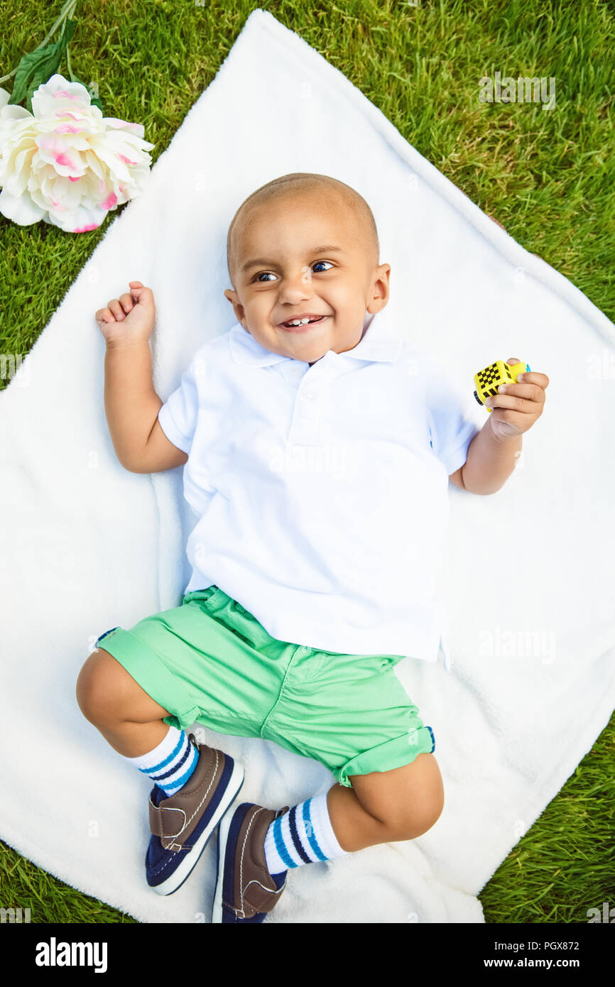 Portrait of cute adorable smiling laughing little indian mixed race south asian infant boy in white shirt and green shorts pants laying on white blank Stock Photo