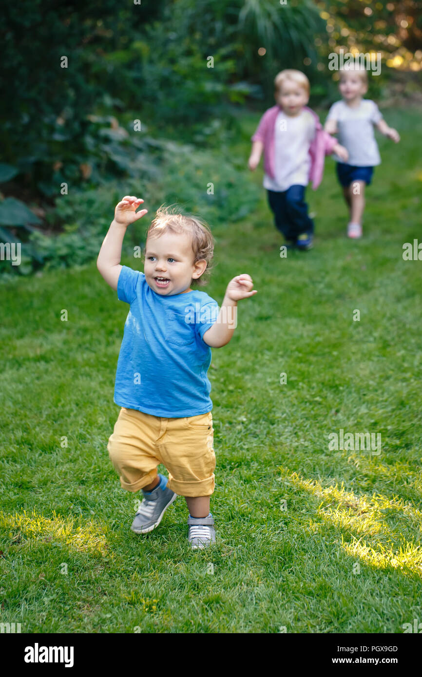 Group portrait of three white Caucasian blond adorable cute kids playing running in park garden outside on bright summer spring day enjoying happy chi Stock Photo