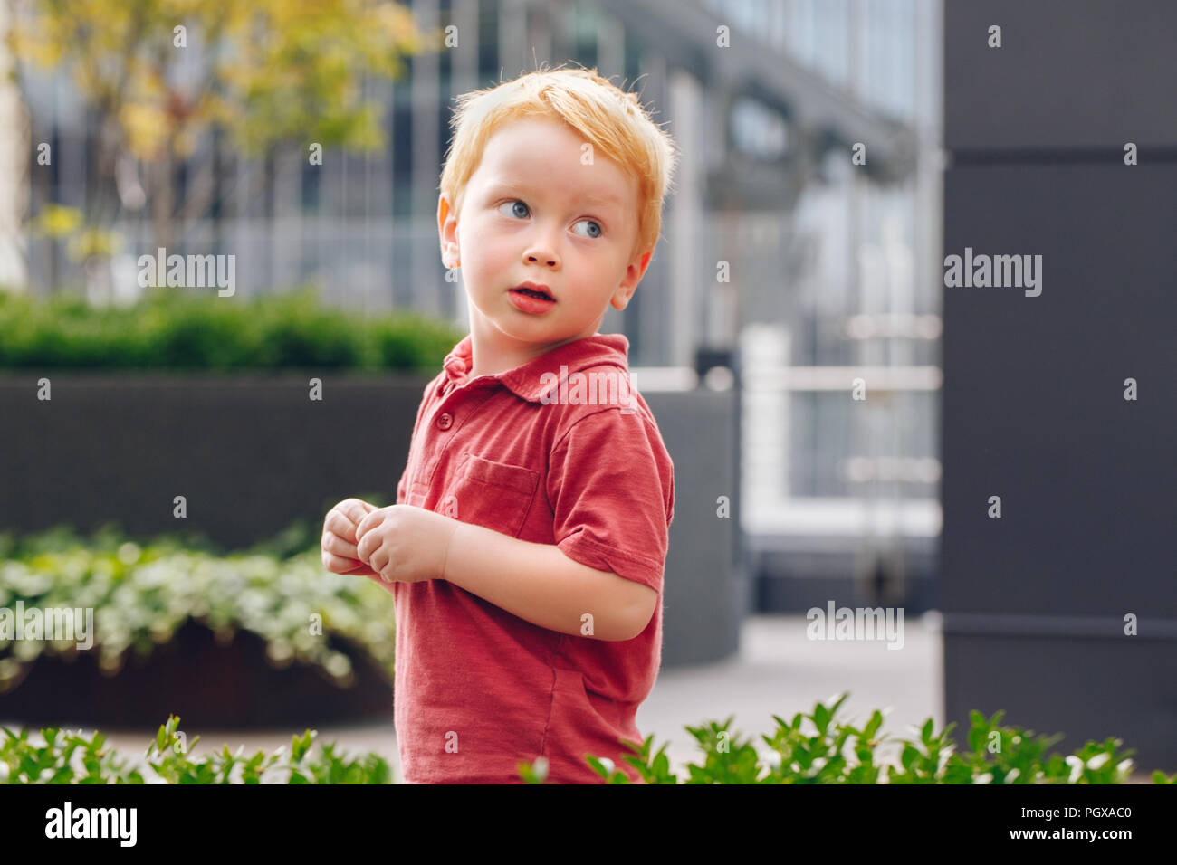Closeup portrait of cute adorable little red-haired Caucasian boy child in red t-shirt standing in park outside looking away. Happy lifestyle childhoo Stock Photo