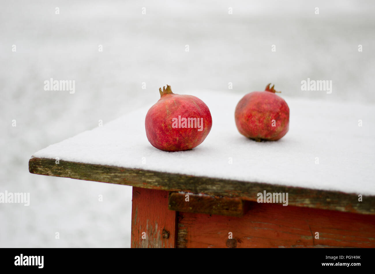 Two red pomegranate on snowy wooden table in winter time Stock Photo