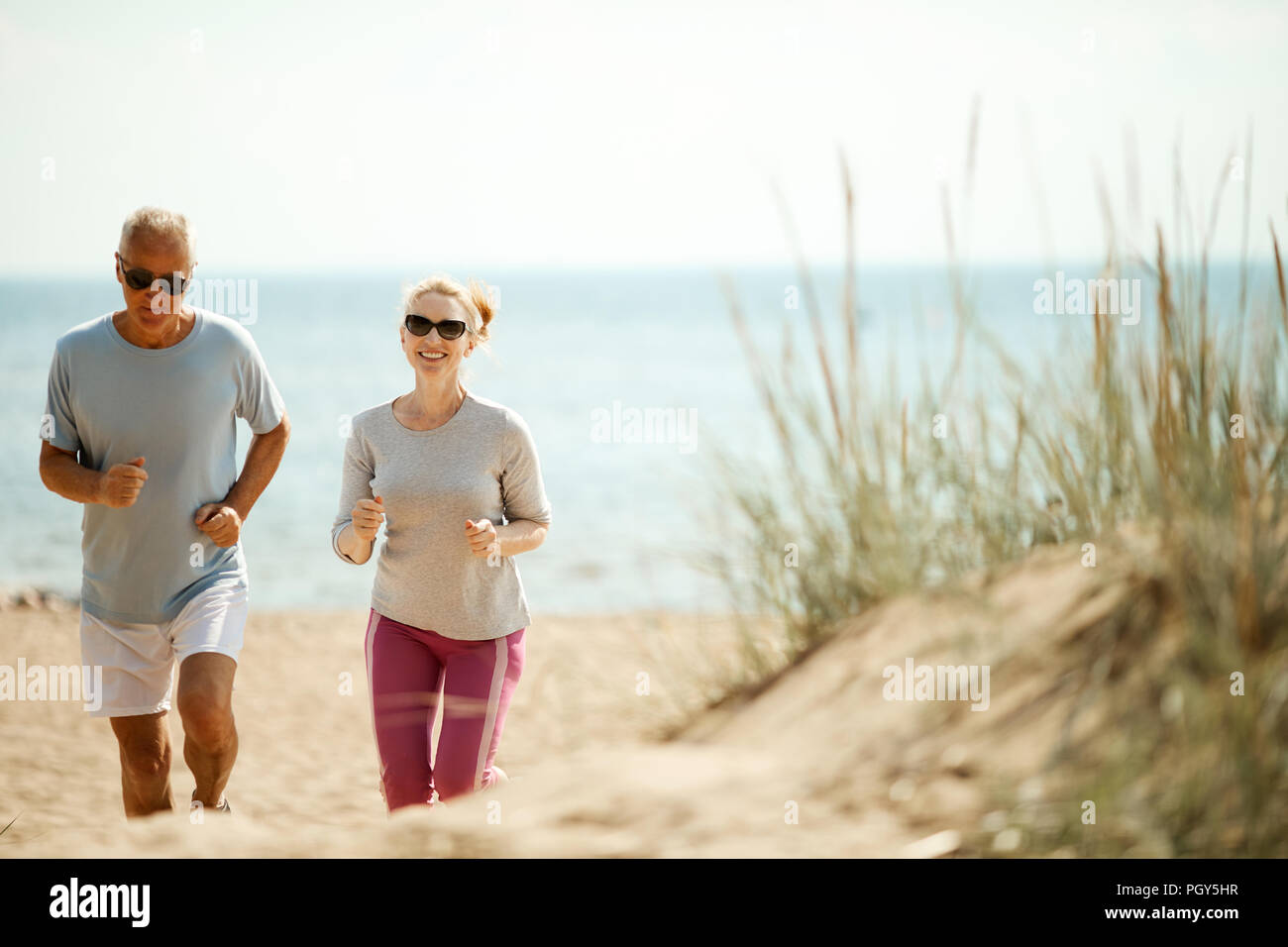 Cheerful and active couple of retired spouses jogging in the morning on the beach Stock Photo