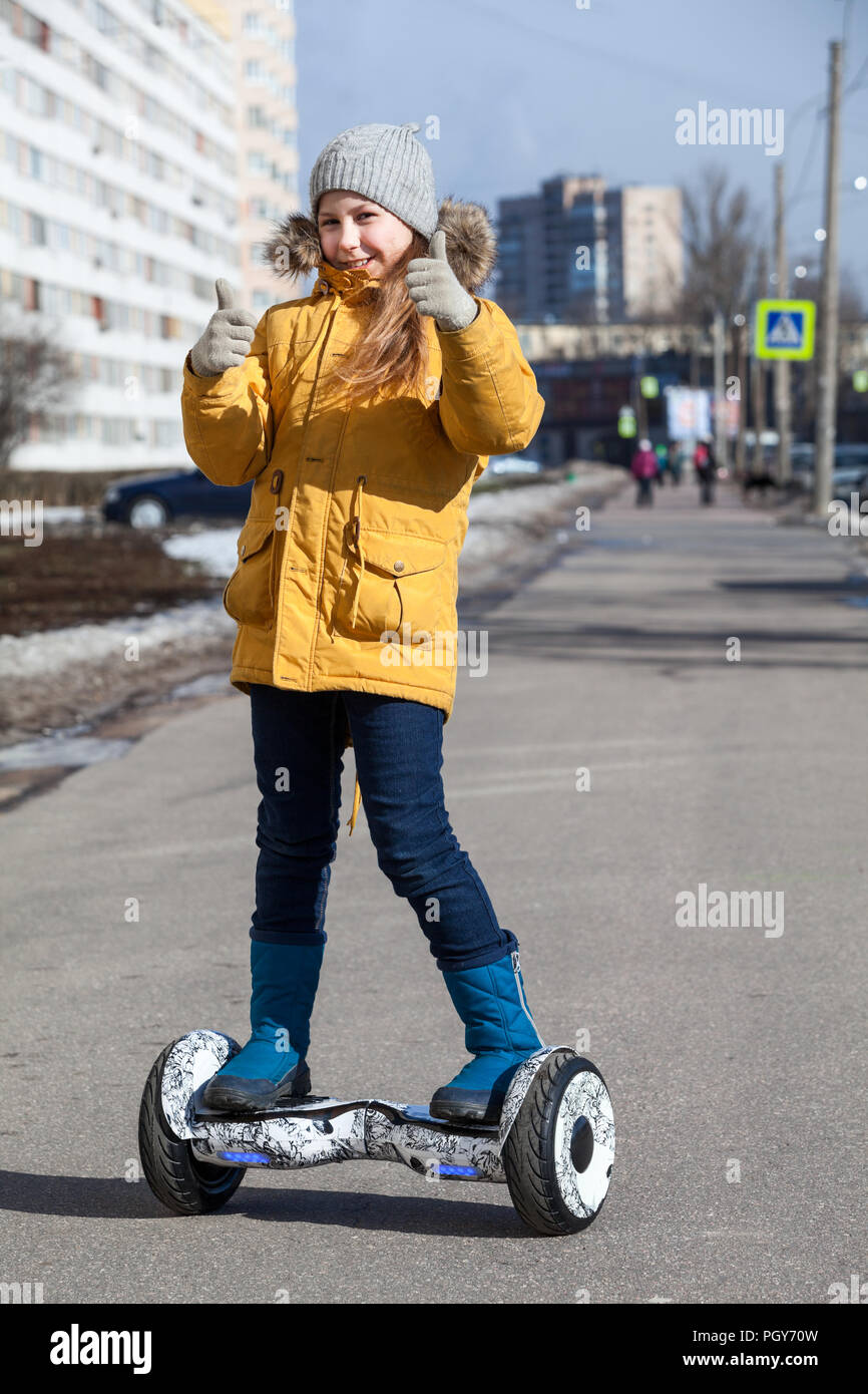 Happy young girl showing thumbs up while driving self-balanced vehicle on street pathway Stock Photo