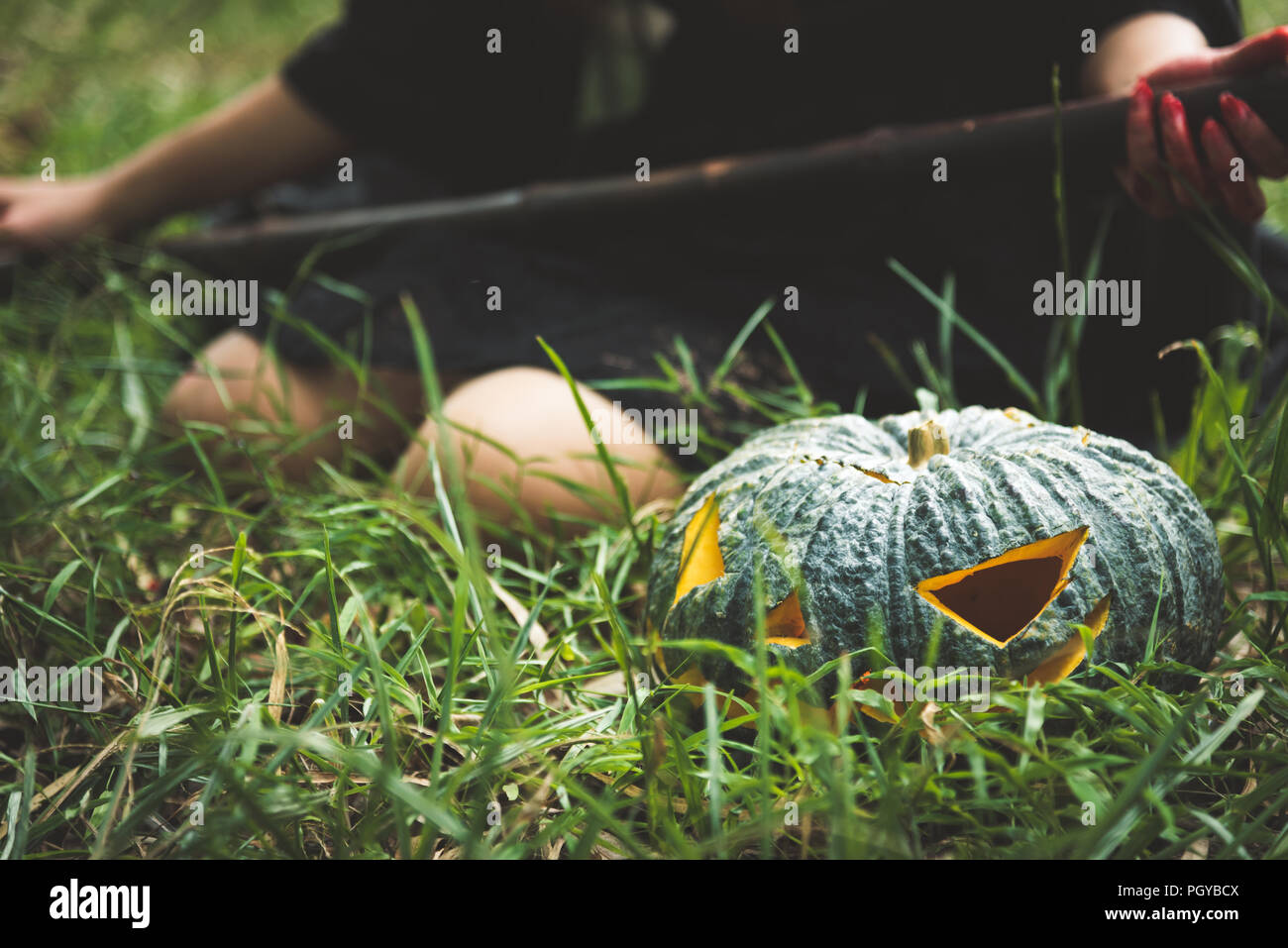 Close up of green pumpkin lantern on grass with female wizard holding magic wand background. Halloween day and horror concept. Cosplay and playful the Stock Photo