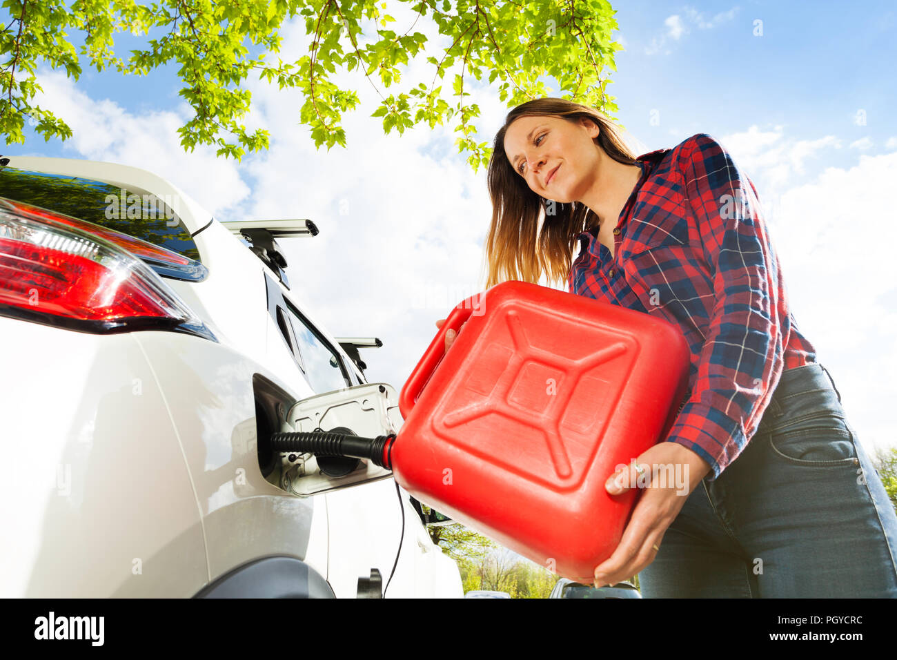 Low-angle shot of beautiful young woman pouring fuel into the gas tank of her car from a red can Stock Photo