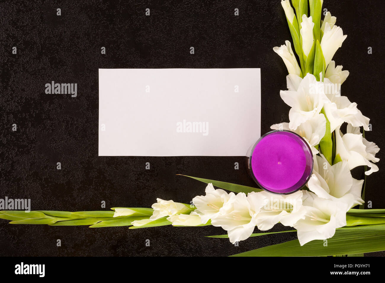 Flowers, empty note and candle on black background, top view. Obituary