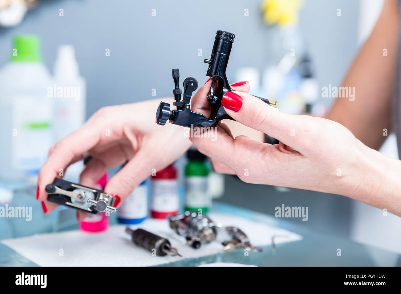 Close-up of the hands of a female artist preparing a professional tattoo machine before tattooing with colored inks in a modern studio Stock Photo