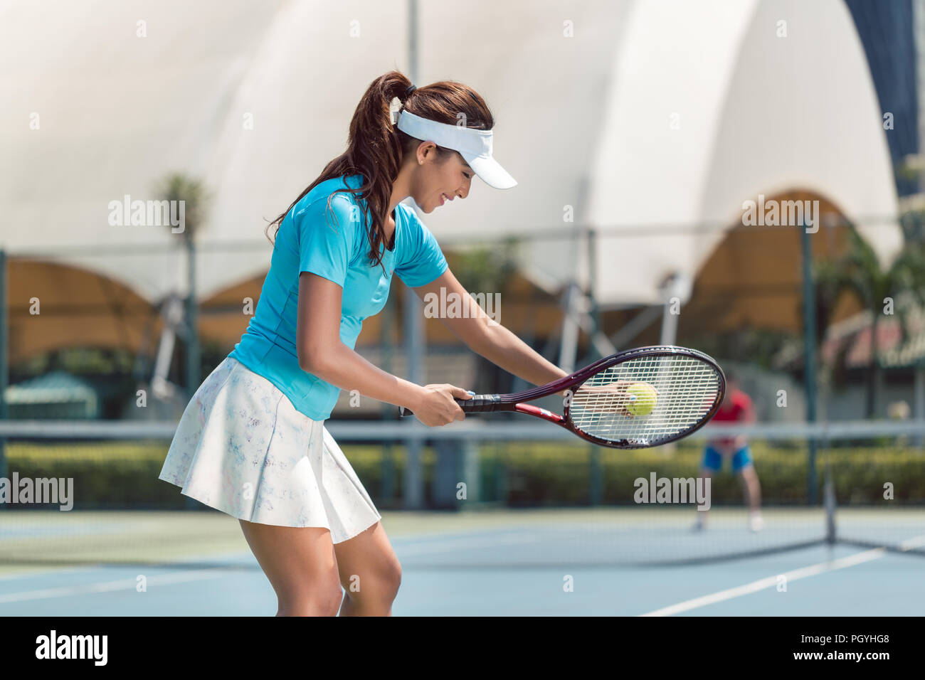 Side view of a beautiful and competitive woman smiling, while holding the tennis racket and the ball before starting the match on a professional tenni Stock Photo