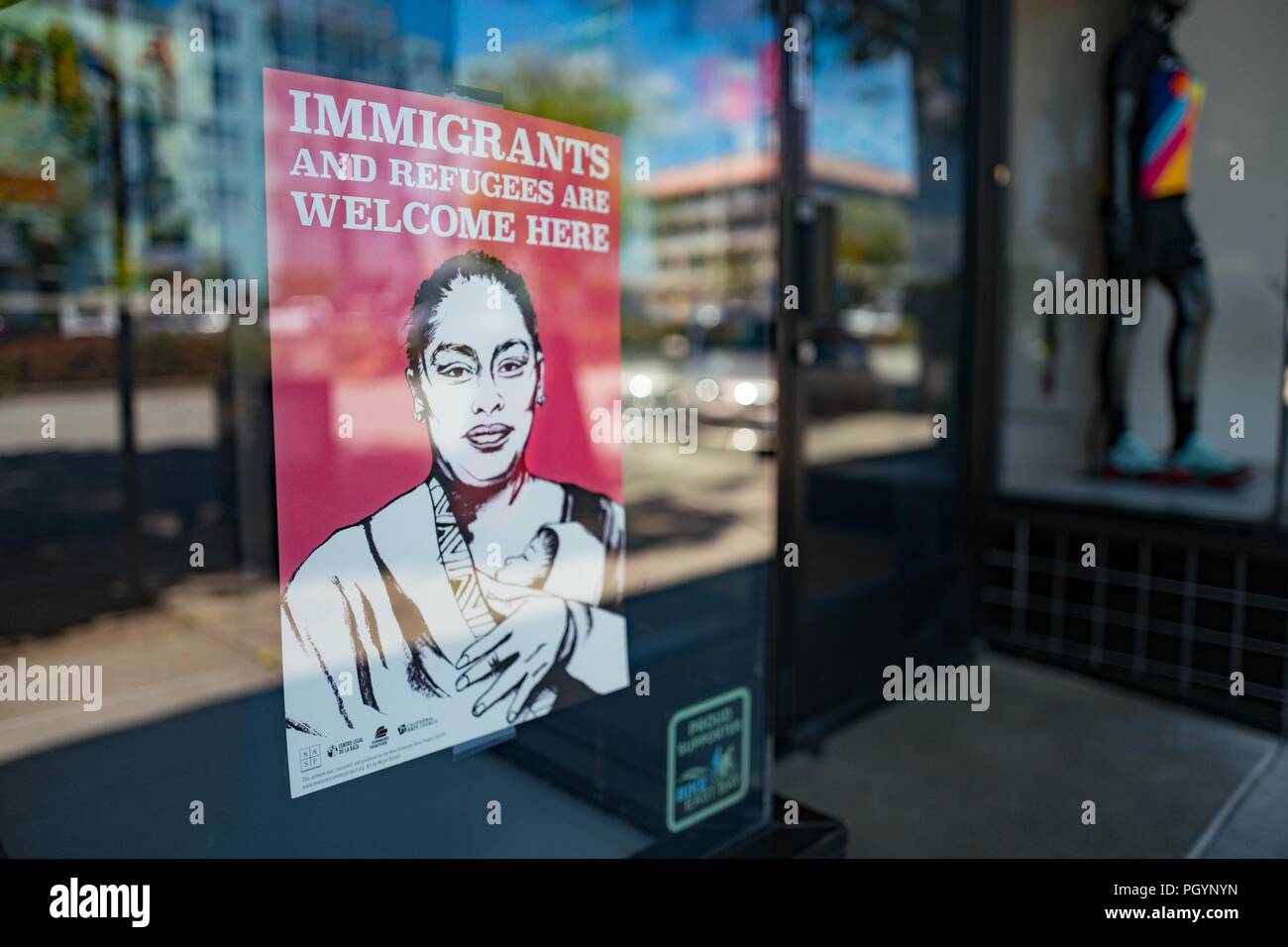 Poster in shop window of a store in downtown Berkeley, California with an image of a woman holding a baby, with text reading Immigrants and Refugees Welcome Here, indicating support of refugee populations who have relocated to the area, May 17, 2018. () Stock Photo