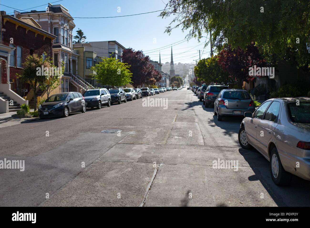View down Valley Street in the Noe Valley neighborhood of San Francisco, California at sundown, with parked cars and Victorian style homes visible, with the spires of Saint Paul's Catholic Church visible in the distance, May 28, 2018. () Stock Photo