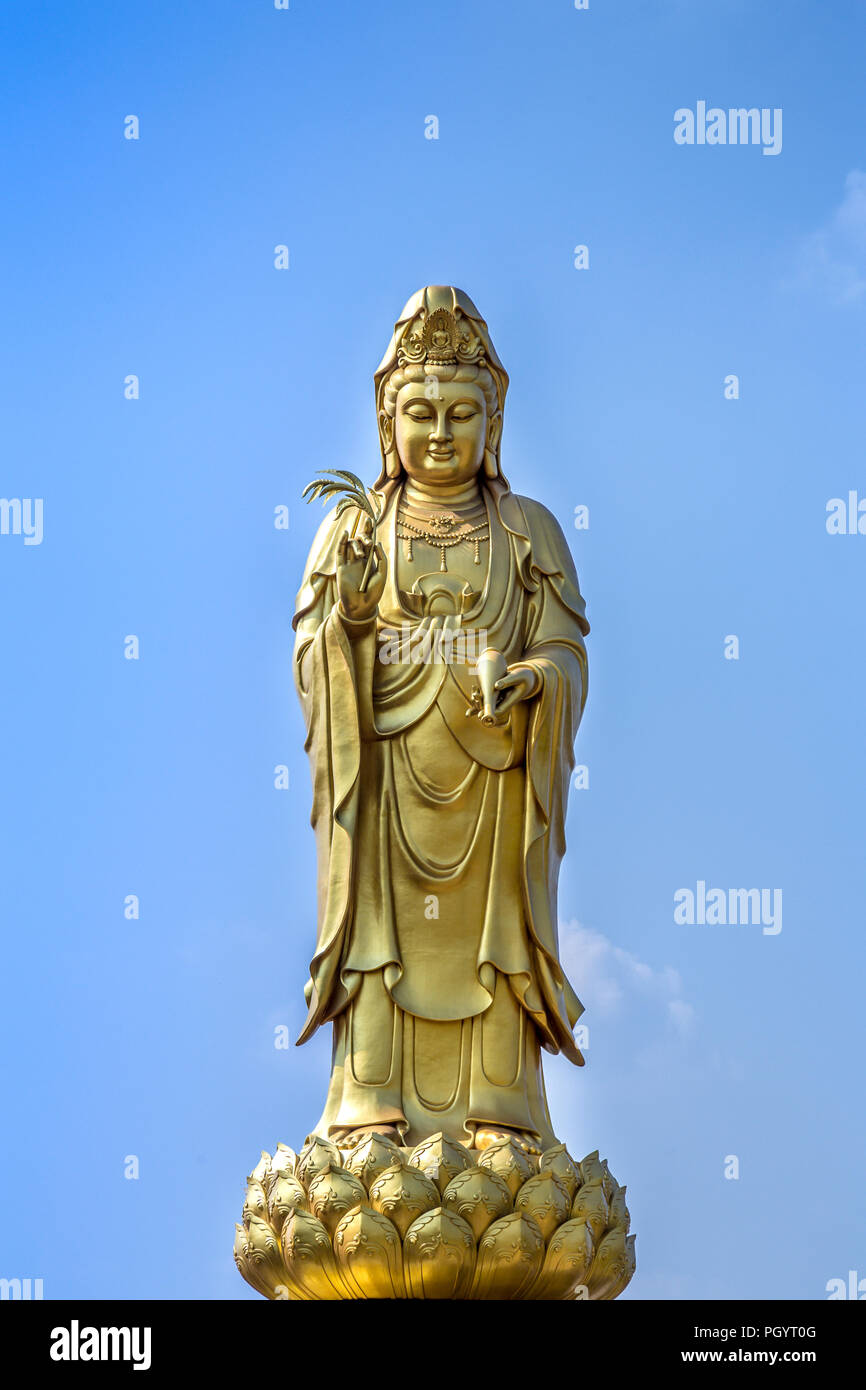 golden statue of the goddess of mercy  guanyin or guan yin standing on the lotus on blue sky background. buddhist and religion concept. Stock Photo