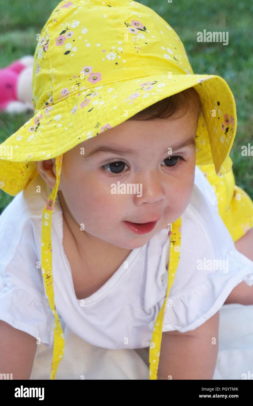Portrait of beautiful and lovely baby girl with brown eyes and yellow hat. Baby playing in the park Stock Photo