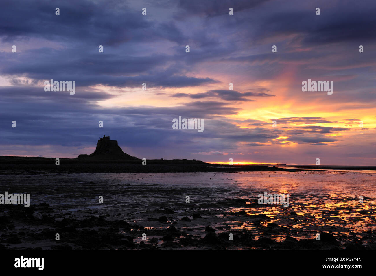 Lindisfarne Castle, Holy Island, seen at dawn as the sun rises over the North Sea, and with low tide in the Lindisfarne harbour, Northumberland. Stock Photo