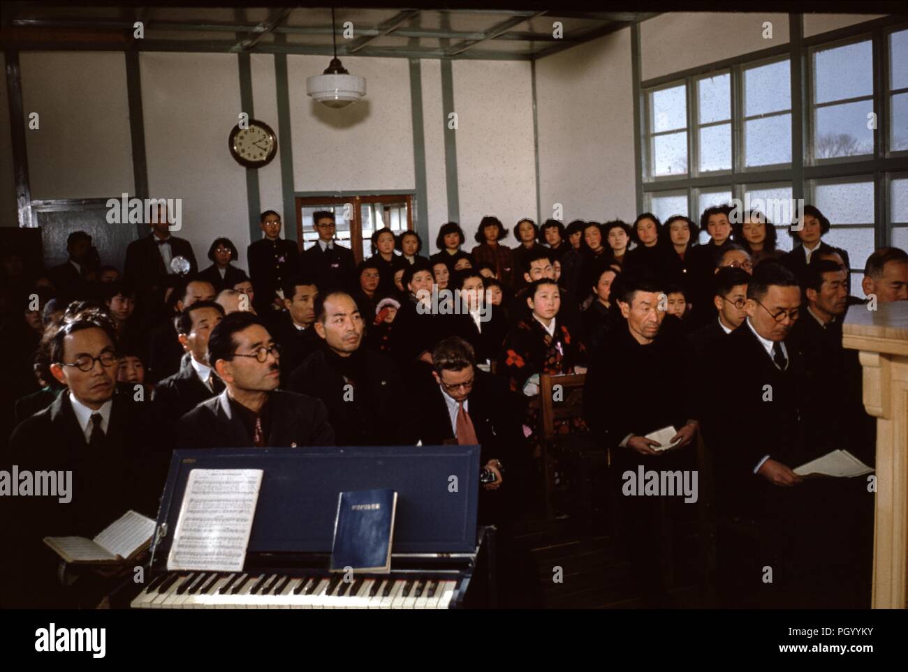 Large group of Japanese people worshiping at a Christian missionary church in post war Japan, with organ and hymn books in the foreground, 1955. () Stock Photo