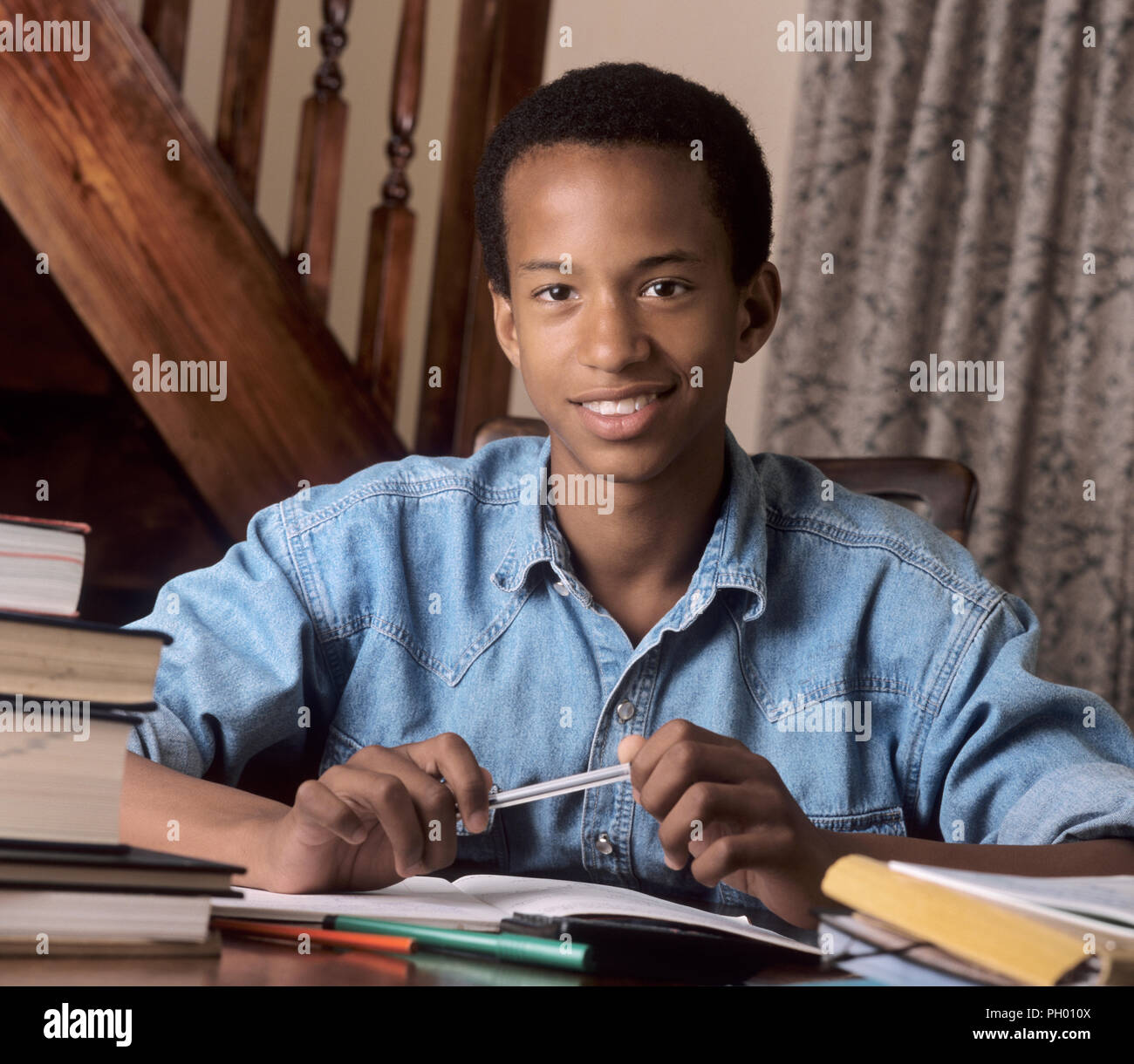 Homework study work & teenage 15-17 yrs black British African Caribbean schoolboy handsome smiling confident doing his homework exam revision at home Stock Photo