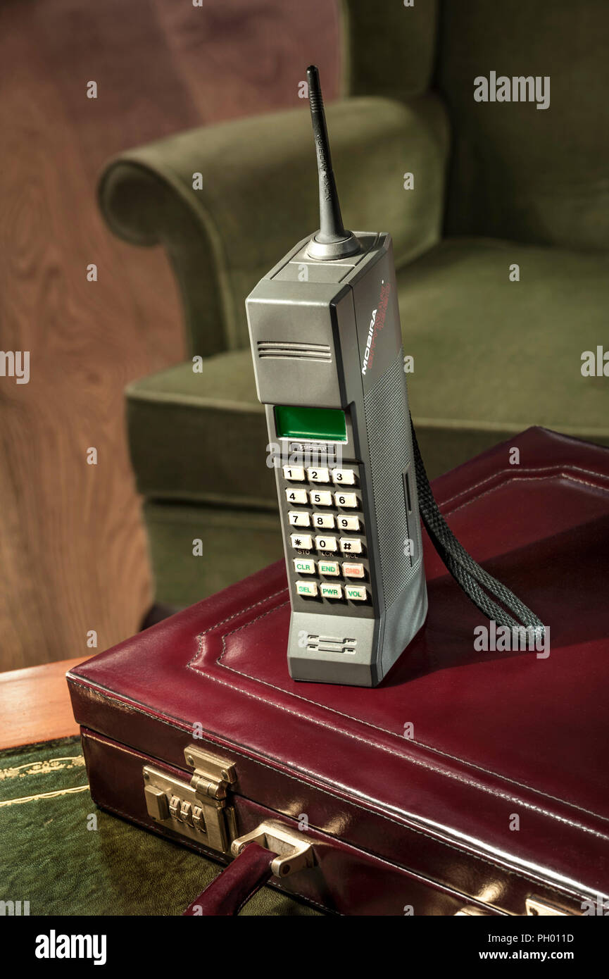 80’s OLD MOBILE CELL PHONE CITYMAN 1987 first generation hand held mobile cell phone Mobira Cityman 1320 with 1980's briefcase desk and office chair Stock Photo