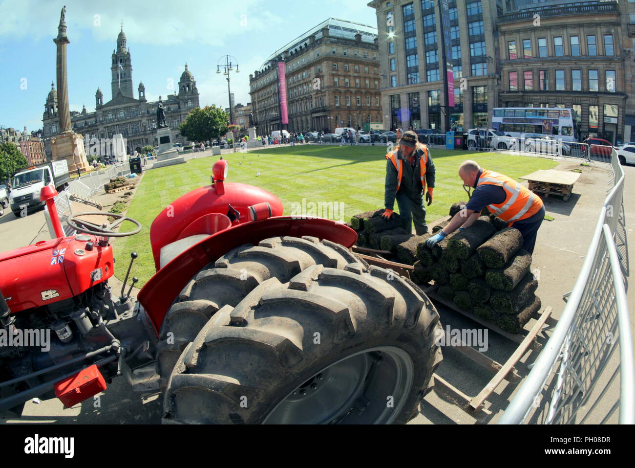 Glasgow, Scotland, UK. 29th  August, 2018. Lunchtime visitors where treated to a bit of living history as a classic  red 1964 Massey Ferguson 35X tractor appeared in the city’s George Square. Locals and tourists watched on as the turf that was lifted for the recent European Championships welcoming centre was replaced. The model sports unusual double wheels to increase traction and was modified by the proud owner pictured. Gerard Ferry/Alamy news Stock Photo