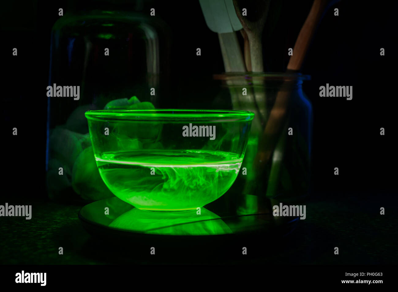 Cooking with chemistry, water filled bowl illuminated by UV light with fluorescent pigment, radiating off eerie lighting glowing in dark radioactive Stock Photo