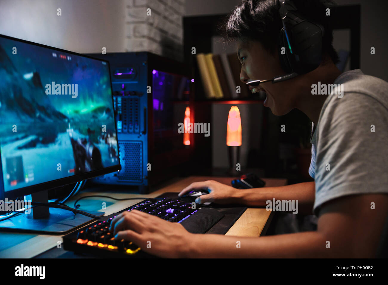 Portrait of asian angry gamer boy playing video games on computer in dark  room wearing headphones and using backlit colorful keyboard Stock Photo -  Alamy