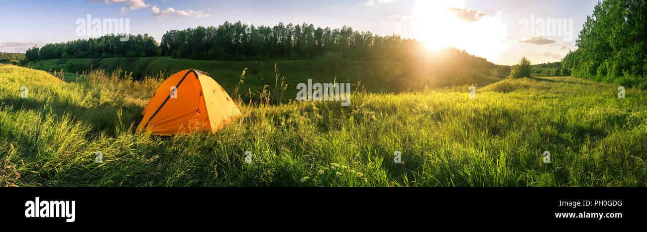 Orange tent in field against background of forest Stock Photo