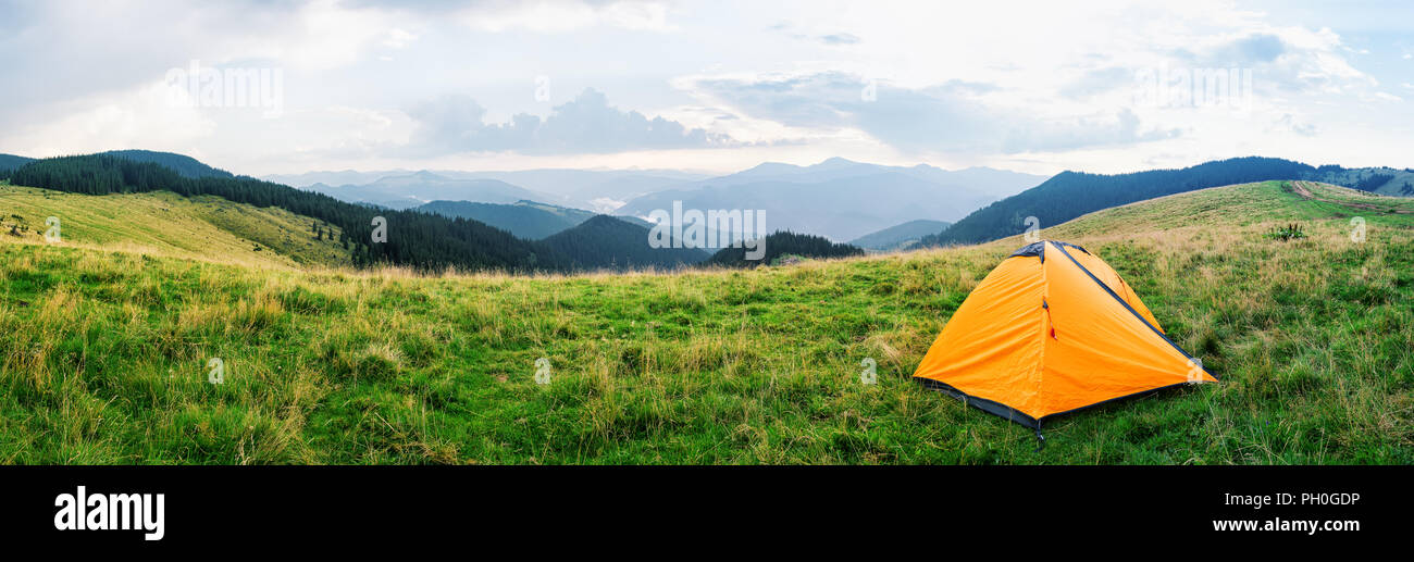 Orange tent on a meadow with green grass in mountains Stock Photo