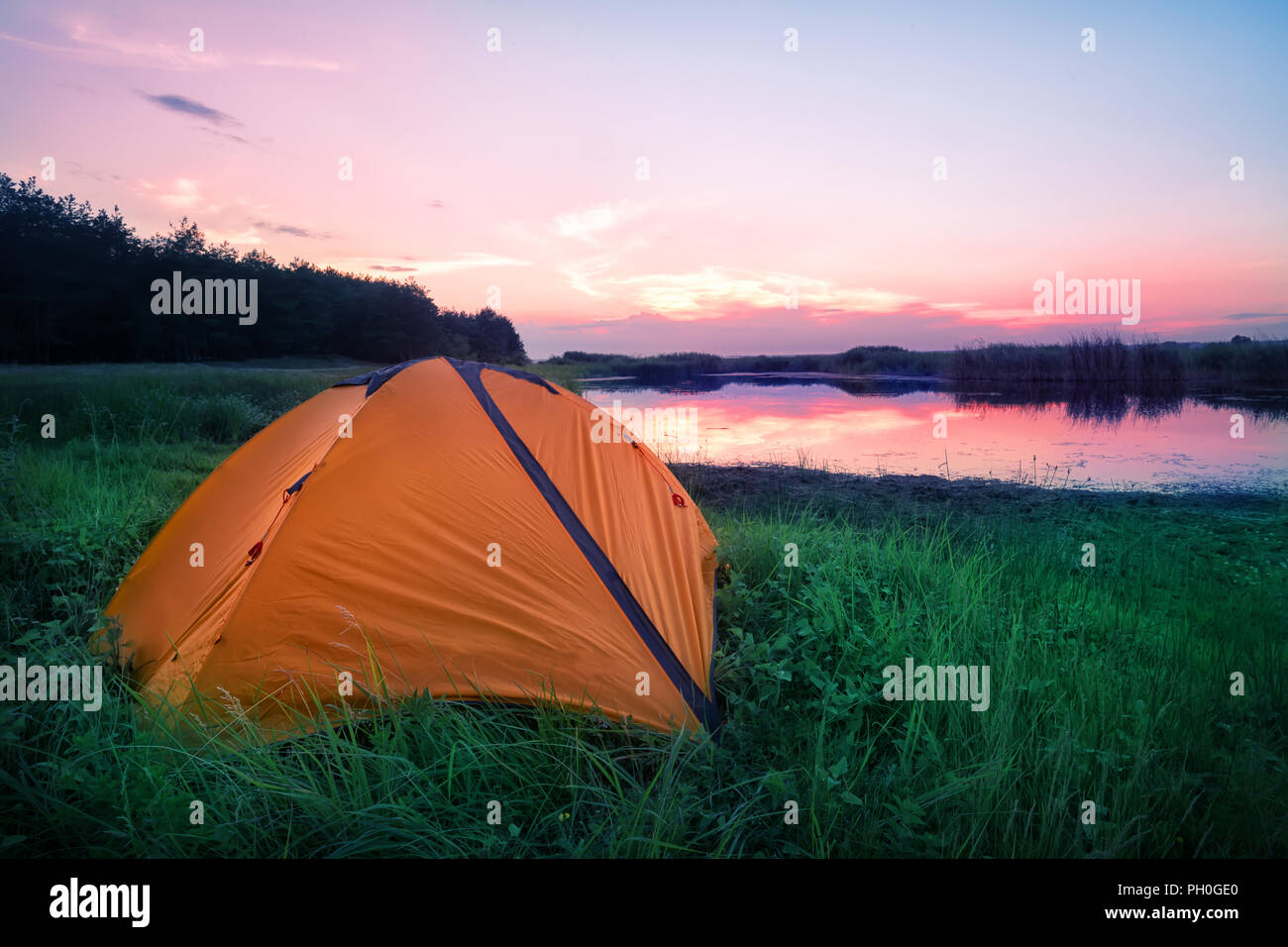 Orange tourist tent in green grass on the lake shore Stock Photo