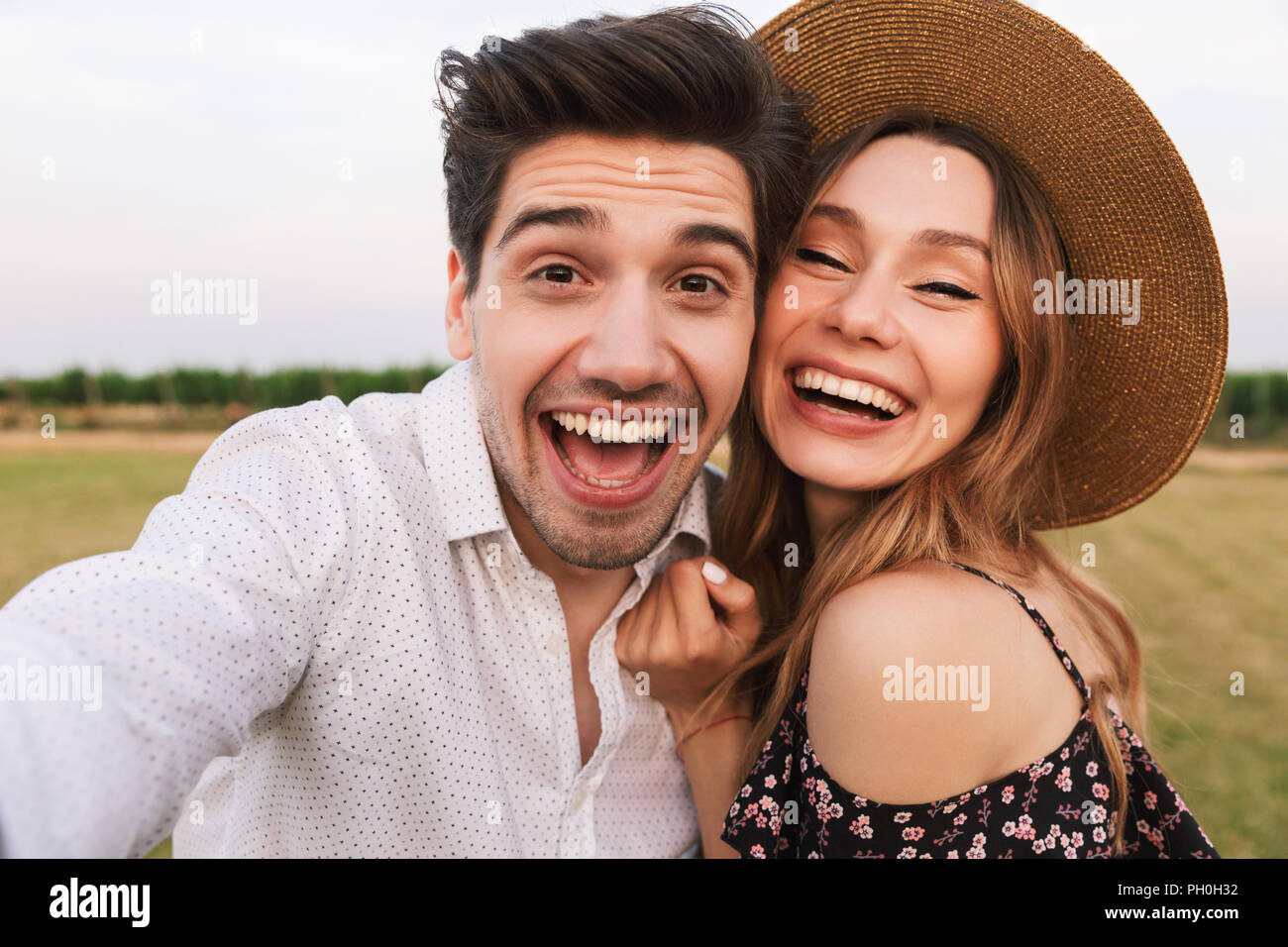 Photo of joyous young man and woman laughing and taking selfie together ...