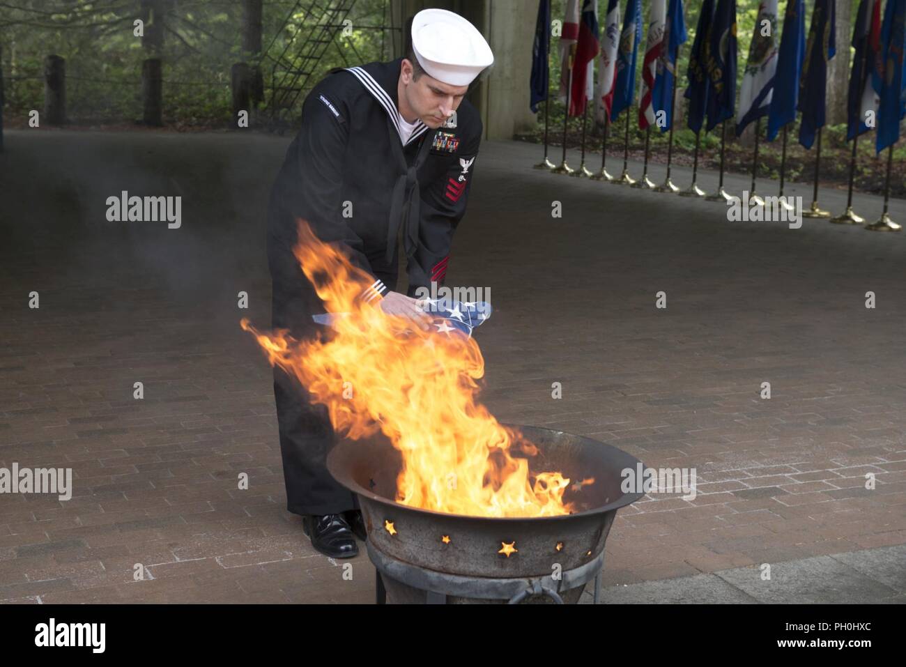 BANGOR, Wash. (June 14, 2018) Machinery Repairman 1st Class David Sams, from East Haddam, Connecticut, assigned to Trident Training Facility in Bangor, Wash., places the remains of a U.S. flag to a fire during a flag retirement ceremony at Naval Base Kitsap-Bangor. When a U.S. flag becomes worn, torn, faded, or badly soiled, it should be retired with the dignity and respect befitting it. BANGOR, Wash. (June 14, 2018) Musician 1st Class Chris Hodges, from Tuscaloosa, Alabama, assigned to Navy Band Northwest, plays the trumpet during a flag retirement ceremony at Naval Base Kitsap - Bangor. When Stock Photo