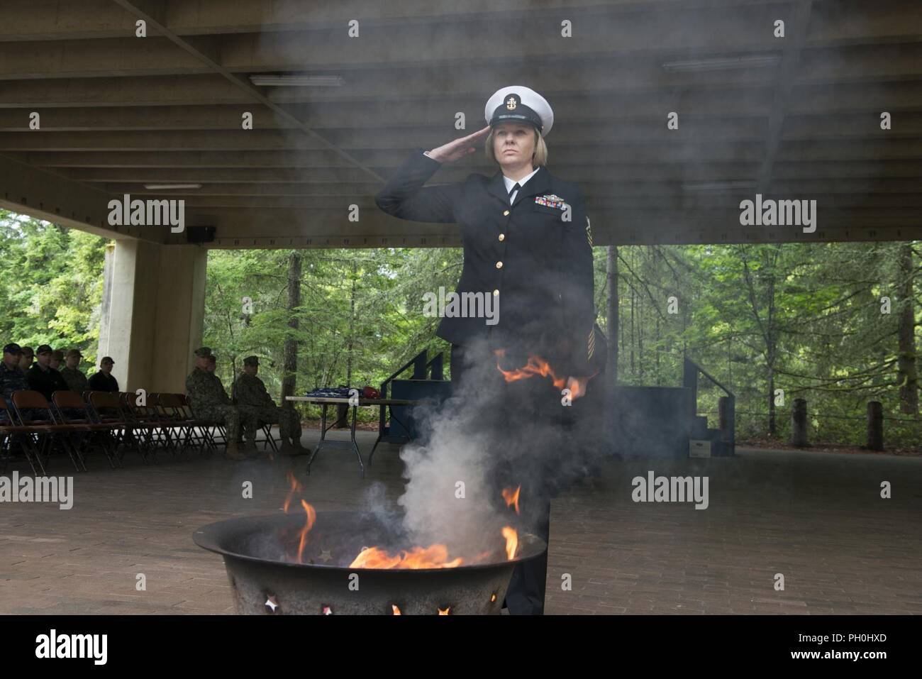 BANGOR, Wash. (June 14, 2018) Chief Hospital Corpsman Farrah Ocasio, from Detroit, Michigan, assigned to Trident Training Facility in Bangor, Wash., renders a salute after placing the remains of a U.S. flag into a fire during a flag retirement ceremony at Naval Base Kitsap-Bangor. When a U.S. flag becomes worn, torn, faded, or badly soiled, it should be retired with the dignity and respect befitting it. BANGOR, Wash. (June 14, 2018) Musician 1st Class Chris Hodges, from Tuscaloosa, Alabama, assigned to Navy Band Northwest, plays the trumpet during a flag retirement ceremony at Naval Base Kitsa Stock Photo