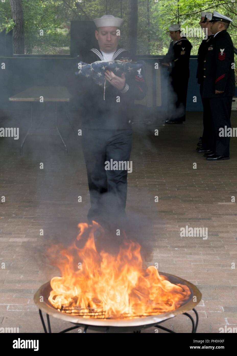 BANGOR, Wash. (June 14, 2018) Sonar Technician 1st Class Ryan Gartley, from Orlando, Florida, assigned to Trident Training Facility in Bangor, Wash., walks the remains of a U.S. flag to a fire during a flag retirement ceremony at Naval Base Kitsap - Bangor. When a U.S. flag becomes worn, torn, faded, or badly soiled, the flag should be retired with the dignity and respect befitting it. The traditional method is to cut the flag into pieces, separating the 13 stripes from canton and incinerating them separately in a respectful manner. Stock Photo