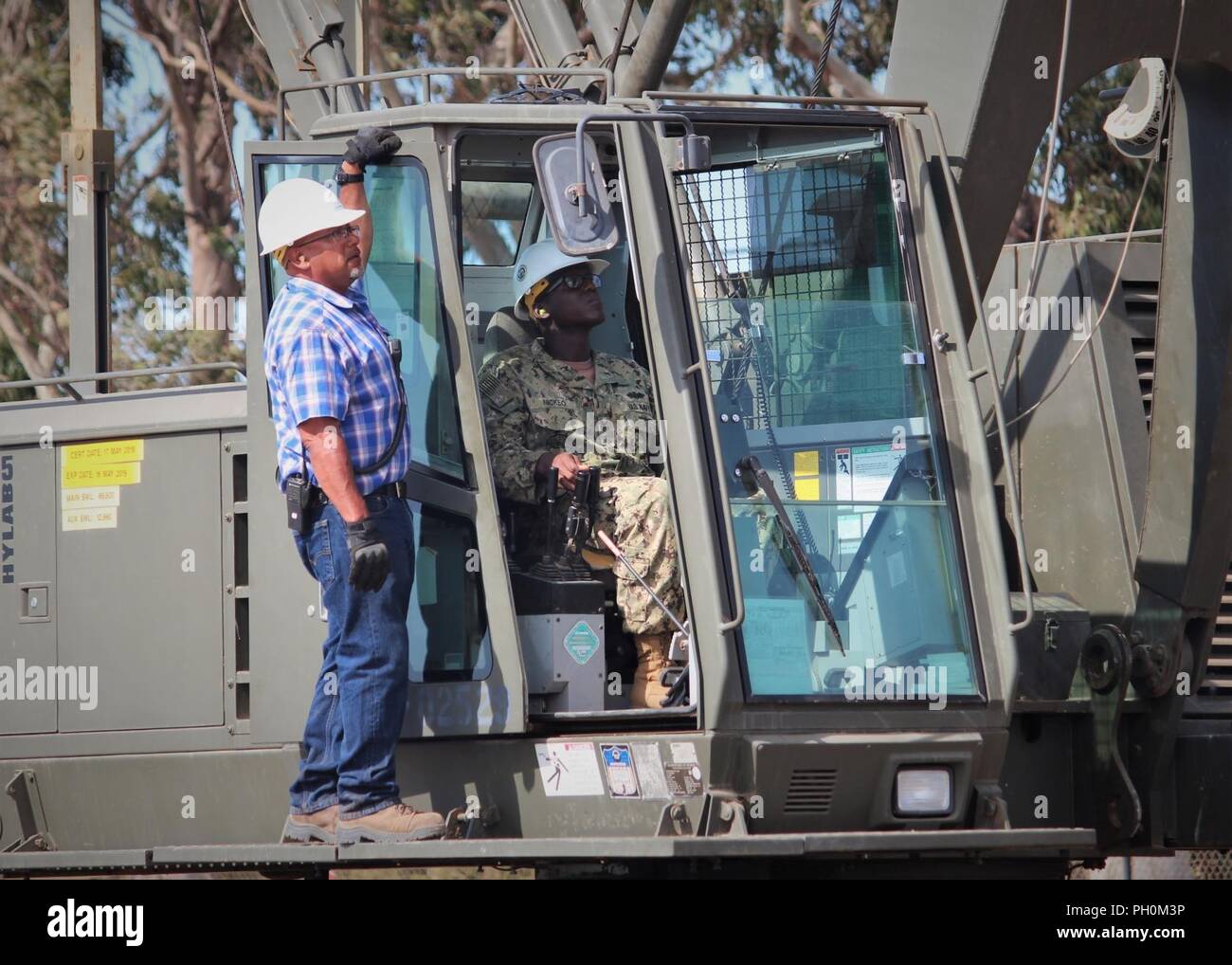 HUENEME, Calif. (June 14, 2018) Naval Construction Training Center “C” school student Equipment Operator 1st Class William Nickeo operates a 50-ton lattice boom crawler crane during hands-on practice with pile driving operations, while instructor Max Lopez supervises. The pile driving operations “C” school course is a module of the crane operator pipeline and teaches equipment operators and construction mechanics how to safely drive and extract piles at the basic level in normal field conditions. Working with timber piles, which are used for building piers and timber bridges, is phase one of t Stock Photo
