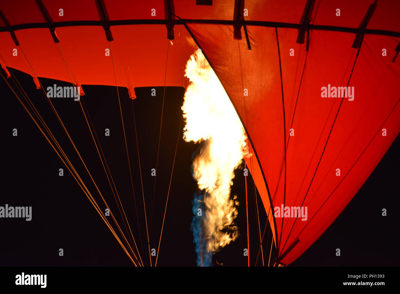 Close-up of a part of red hot air balloon burner flame glowing at night, burner with a extreme hot flame light up the inside of a red hot air balloon Stock Photo