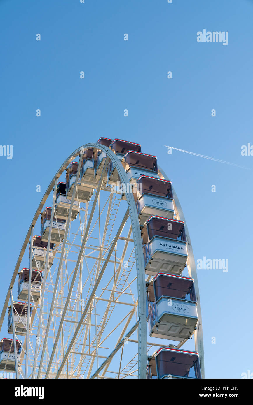 26 August 2018 - Geneva, Switzerland. Vertical image of the Ferris Wheel cabins against the blue sky and flying plane. Stock Photo