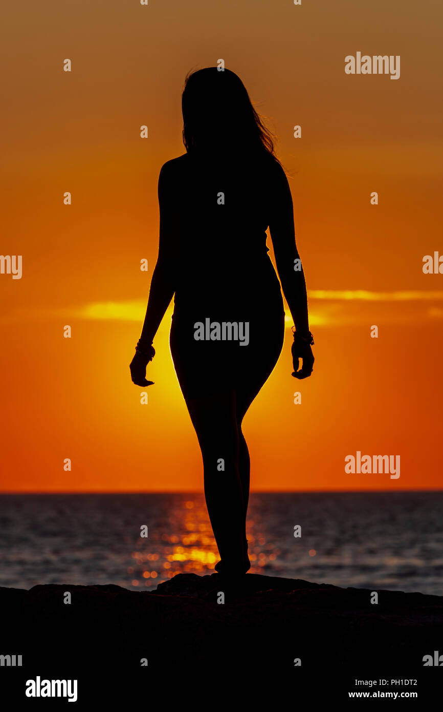 A woman is silhouetted at sunset on the jetty at Menemsha Beach in Chilmark, Massachusetts on Martha's Vineyard. Stock Photo