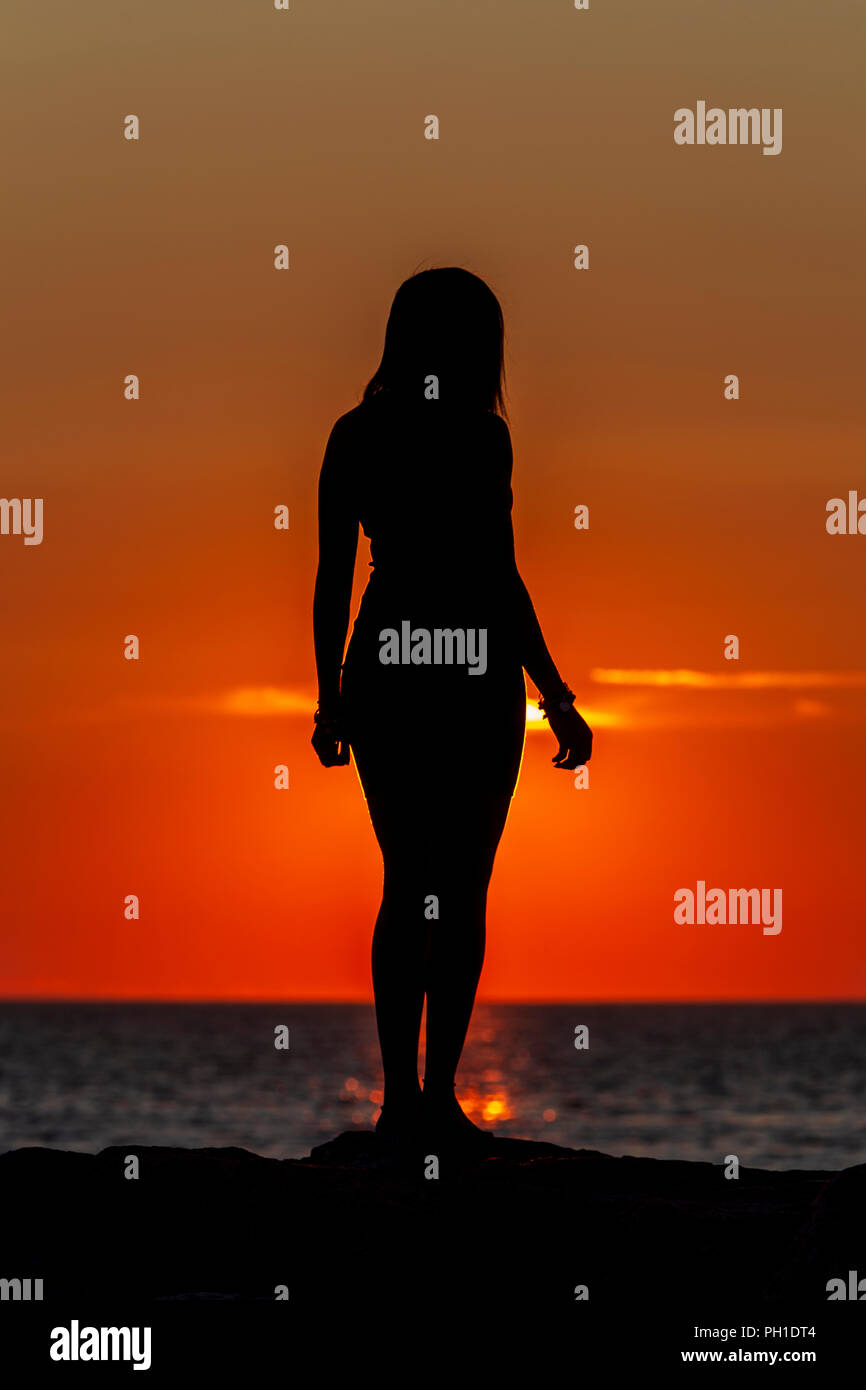 A woman is silhouetted at sunset on the jetty at Menemsha Beach in Chilmark, Massachusetts on Martha's Vineyard. Stock Photo