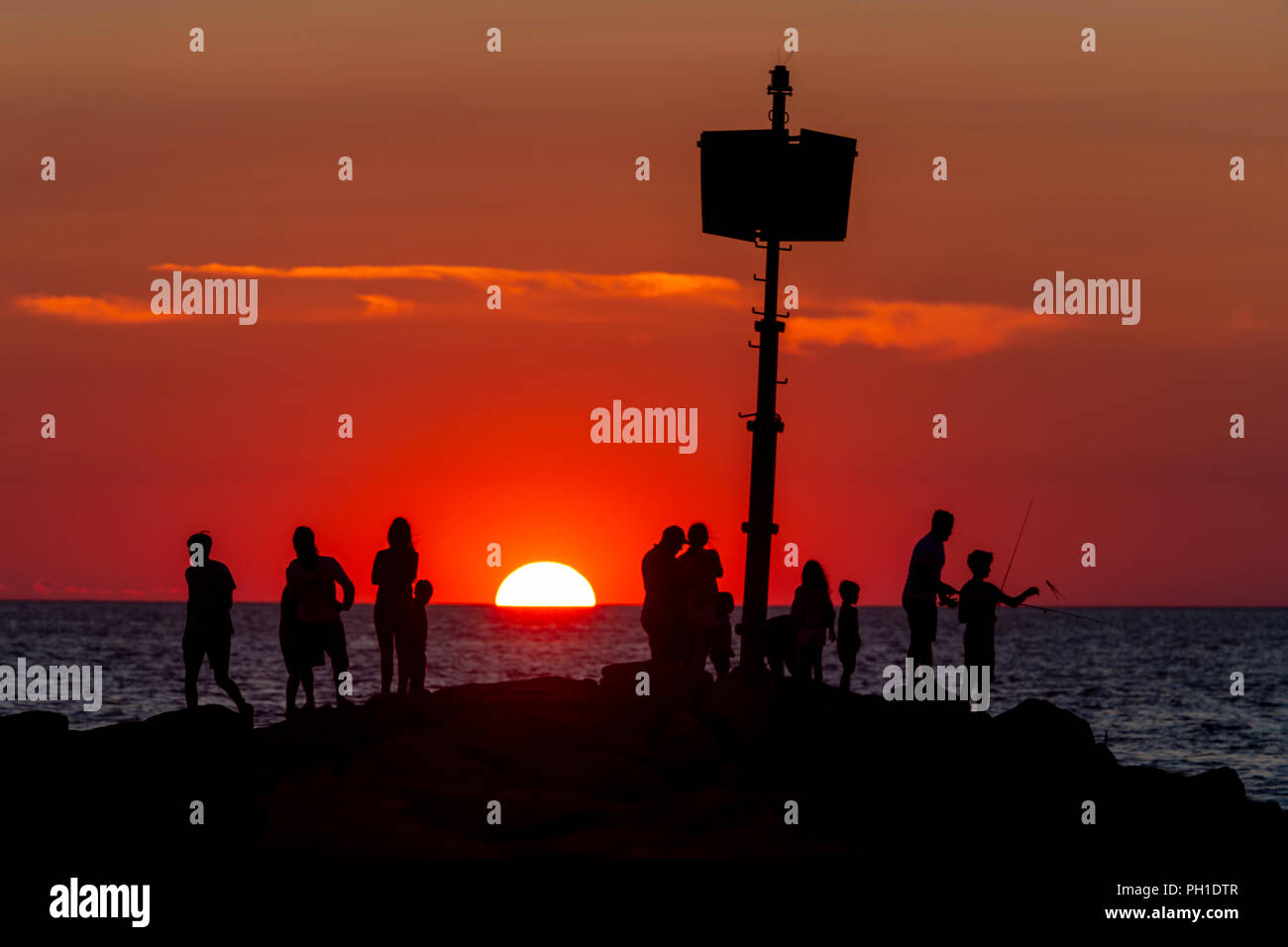 People stand on the jetty, some fishing, and watch the sunset at Menemsha Beach in Chilmark, Massachusetts on Martha's Vineyard. Stock Photo