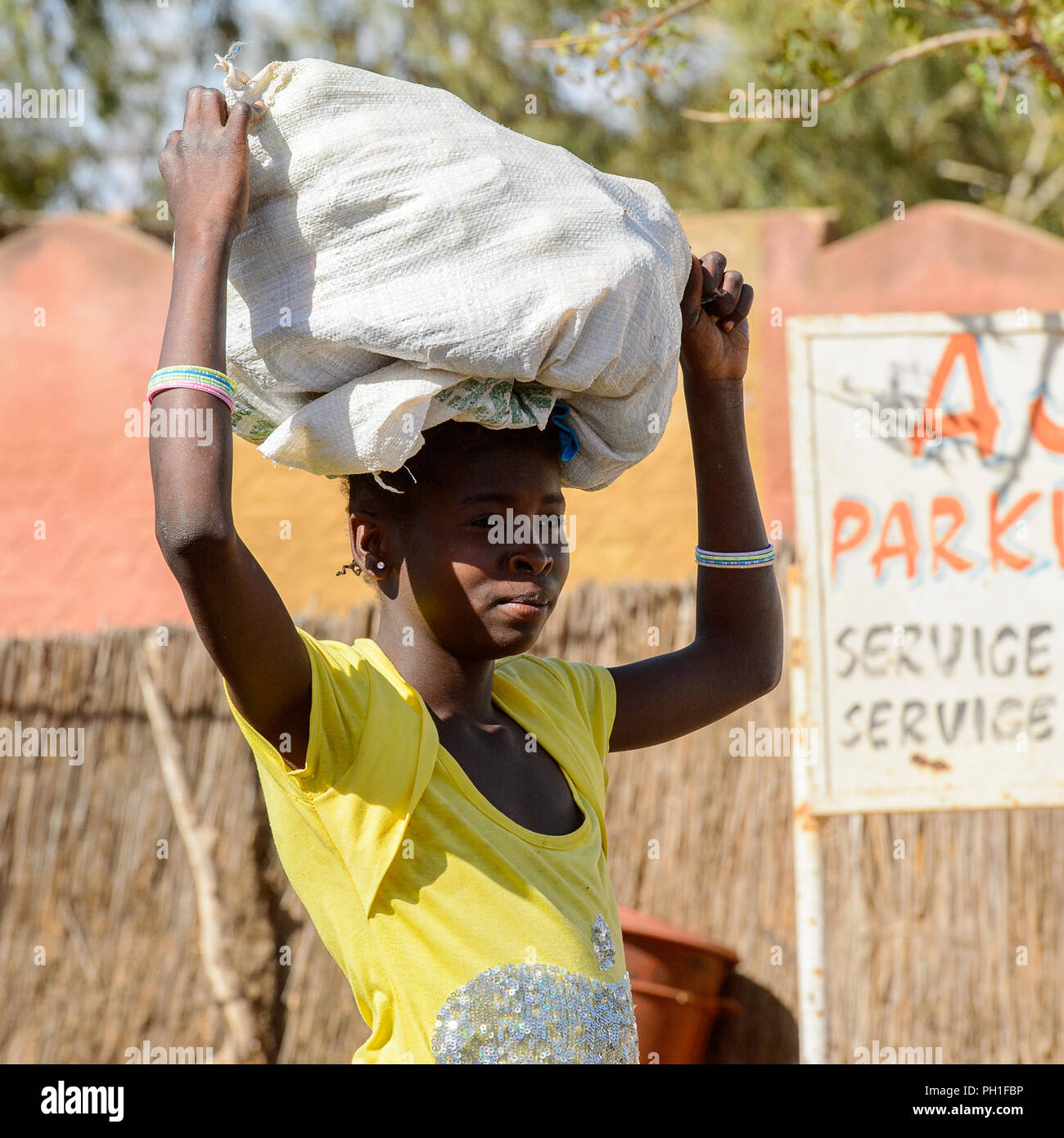 LAMPOUL DESERT village, SENEGAL - APR 23, 2017: Unidentified Senegalese woman carries a bag on her head in a village near the Lampoul Desert Stock Photo