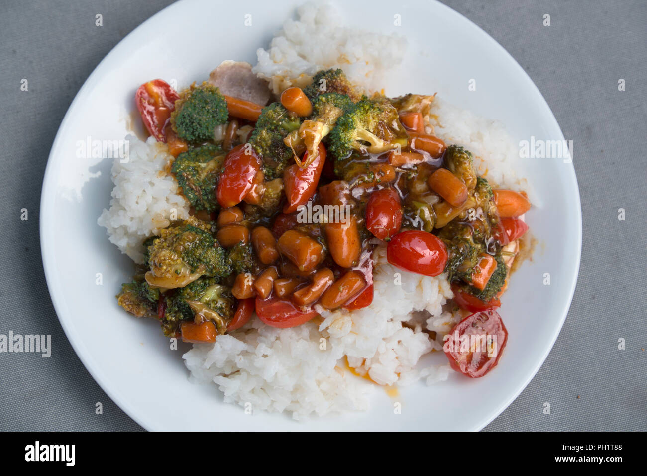 Vegetable stir fry with broccoli, carrots and grape tomatoes served on white, long-grain rice. Stock Photo