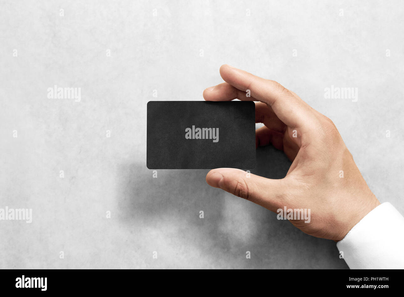 Hand hold blank black craft card mockup with rounded corners. Plain kraft call-card mock up template holding arm. Hand made namecard display front. Ch Stock Photo