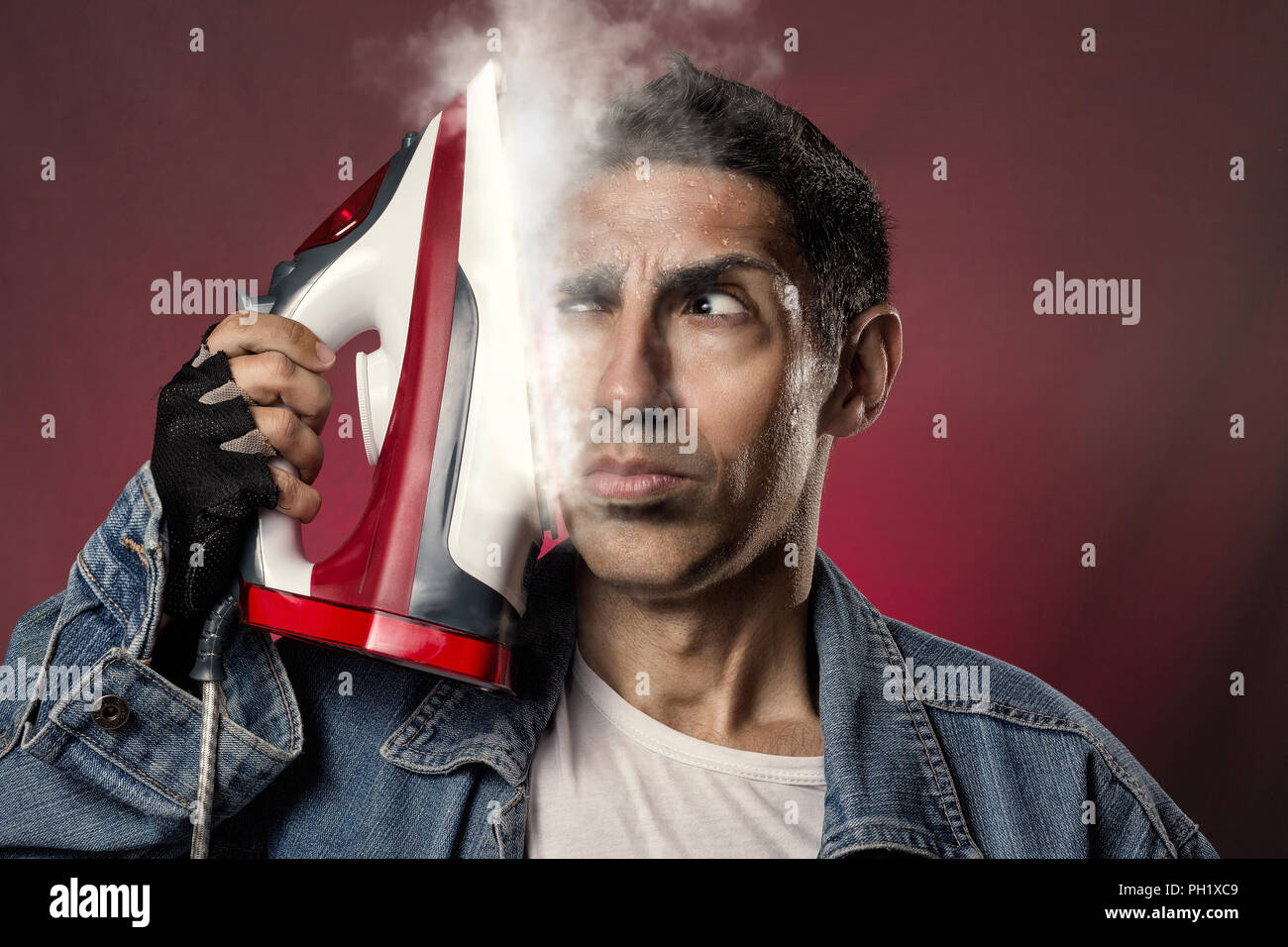 Crazy man ironing his own face with the iron on and emitting steam. Stock Photo