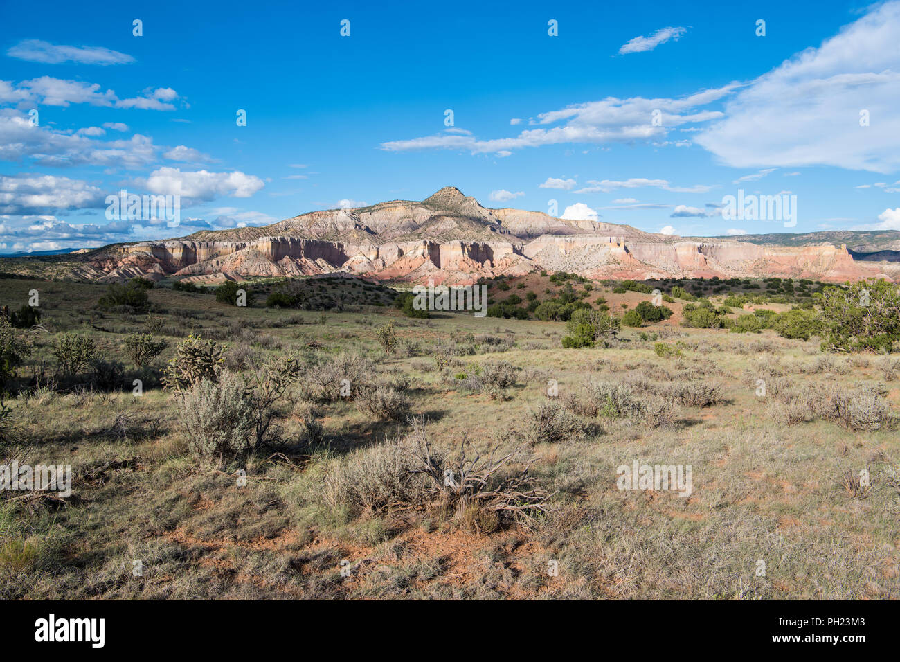Mountain peak, colorful cliffs, and vast desert landscape underneath dramatic blue sky and clouds at Ghost Ranch near Abiquiu, New Mexico Stock Photo