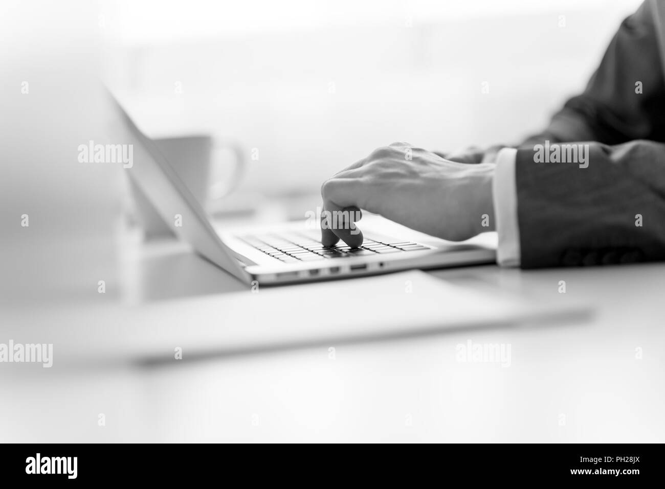 Close up view of the hands of a businessman in a suit typing data on a laptop computer in a selective focus greyscale image. Stock Photo