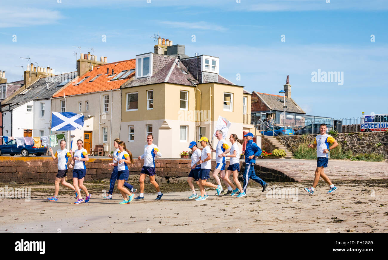 West Bay, North Berwick, East Lothian, Scotland, UK, 30th August 2018. Sir Chinmoy Oneness-Home Peace run runners set off in the sunshine from North Berwick West Bay beach to run along the coastline to Dirleton carrying a flaming peace torch and a saltire and peace flag. The flags and torch are carried by a team of international runners through the United Kingdom over 16 days starting from today. The Peace Run is a global torch relay promoting world peace Stock Photo