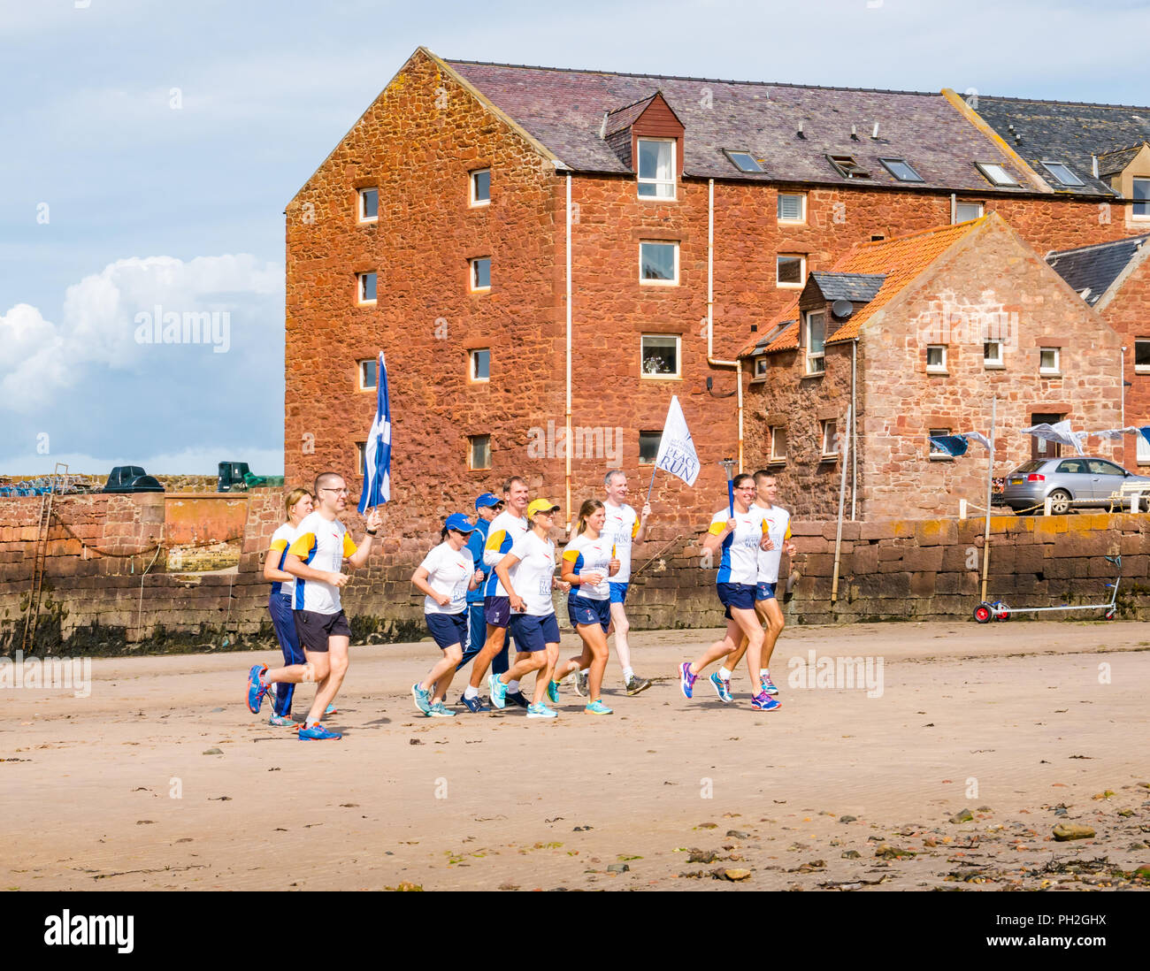 West Bay, North Berwick, East Lothian, Scotland, UK, 30th August 2018. Sir Chinmoy Oneness-Home Peace run runners set off in the sunshine from North Berwick West Bay beach to run along the coastline to Dirleton carrying a flaming peace torch and a saltire and peace flag. The flags and torch are carried by a team of international runners through the United Kingdom over 16 days starting from today. The Peace Run is a global torch relay promoting world peace Stock Photo